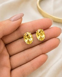 Warm yellow oval crystal earrings shown on hand for size reference with faceted sparkle and silver settings.