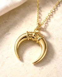Gold celestial horn pendant necklace displayed on white surface with soft luxury lighting