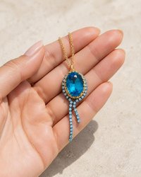 Close-up of a handmade gold necklace with a brilliant blue Swarovski® crystal pendant and sparkling halo design.