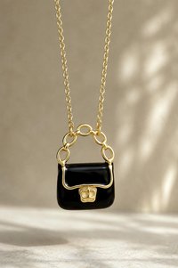 Black enamel purse pendant hanging from delicate gold chain.