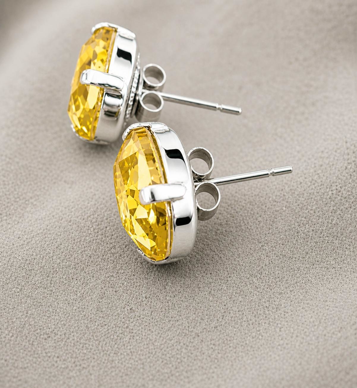 Citrine yellow oval crystal stud earrings in silver plated prong settings displayed on a neutral textured fabric background.