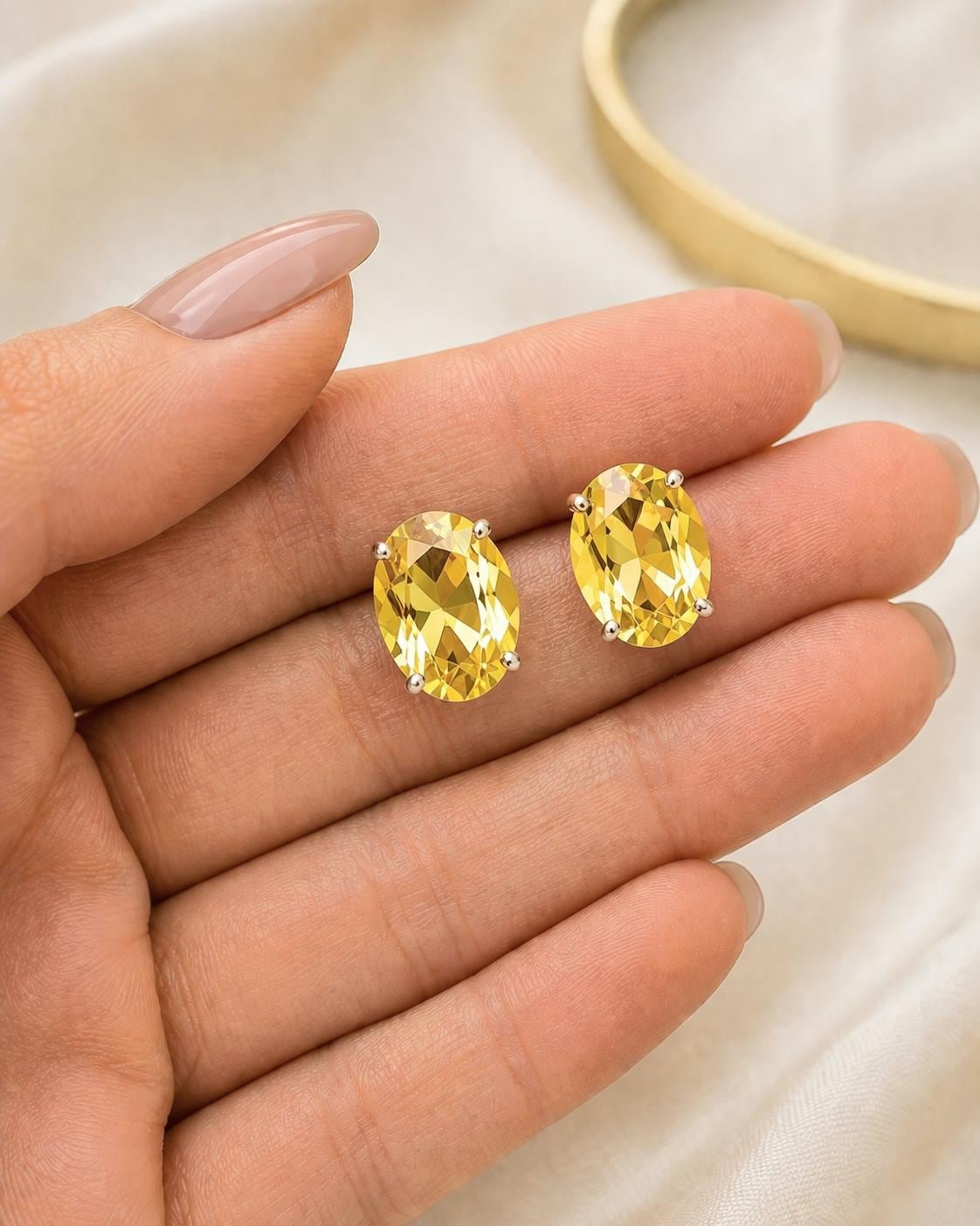 Warm yellow oval crystal earrings shown on hand for size reference with faceted sparkle and silver settings.