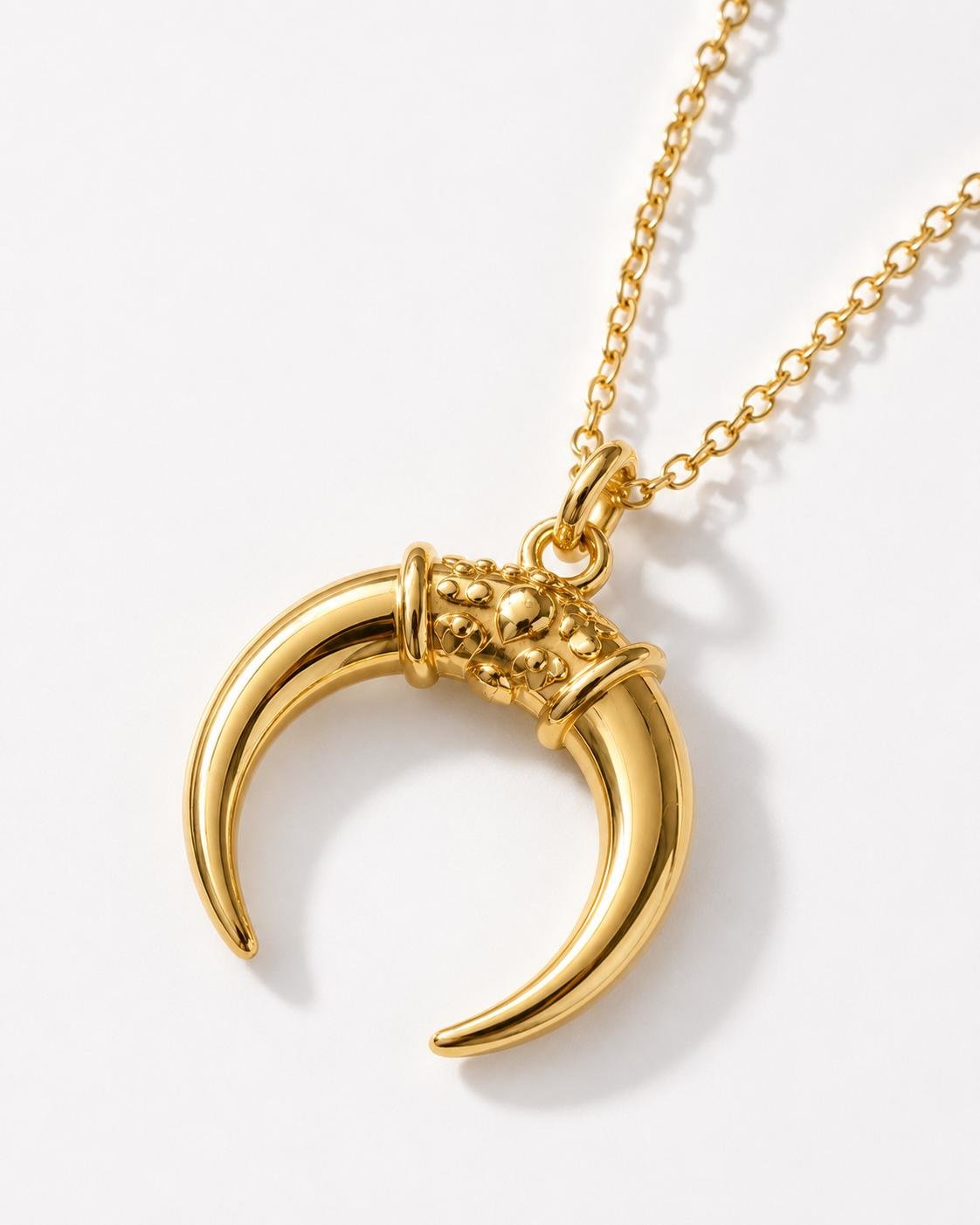 Gold celestial horn pendant necklace displayed on white surface with soft luxury lighting