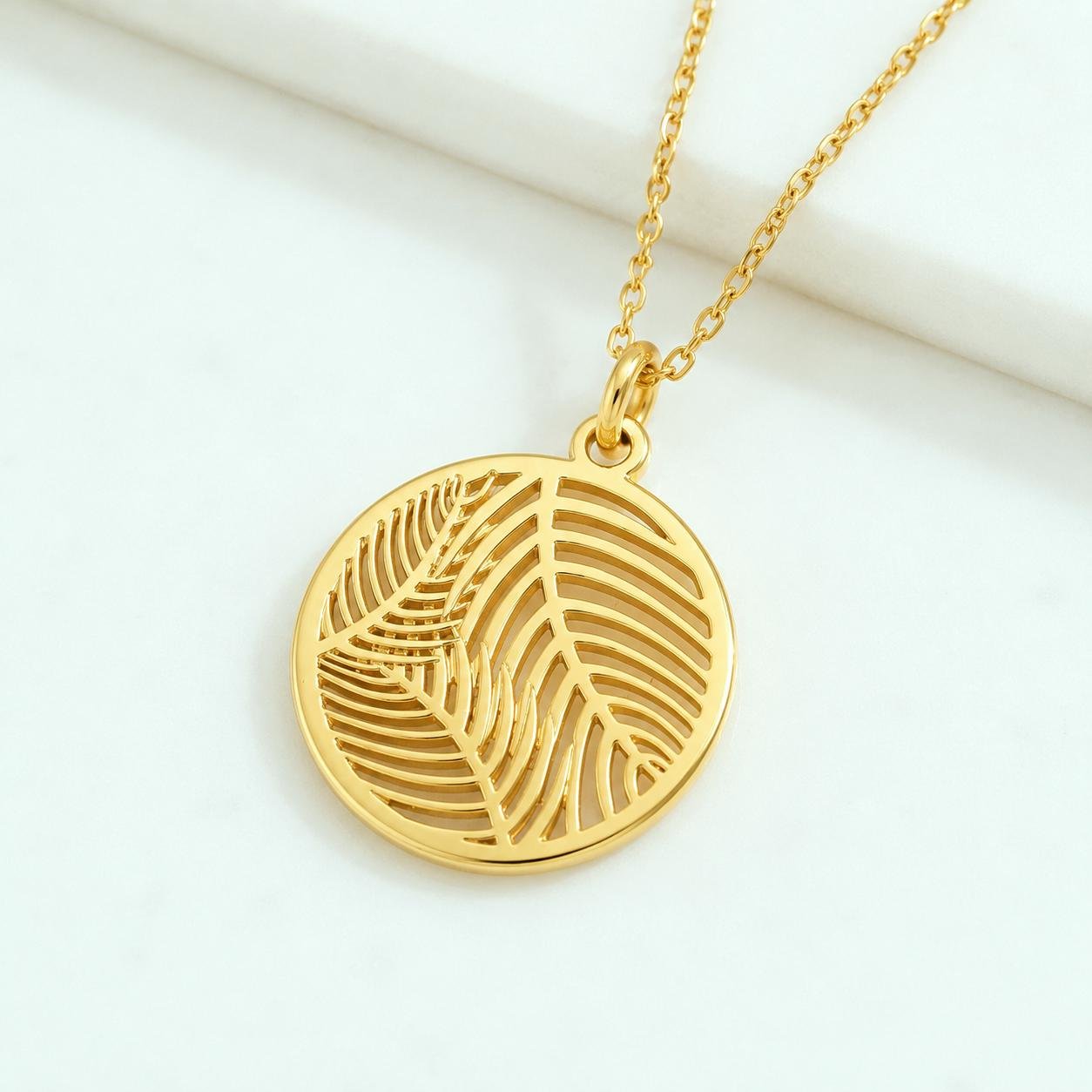 Gold palm leaf pendant necklace hanging on white background with soft lighting