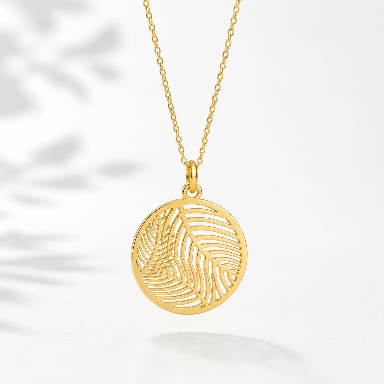 Gold palm leaf pendant necklace hanging on white background with soft lighting