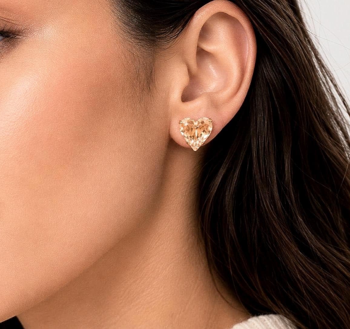 Model wearing a 13mm gold plated heart crystal stud earring made with Swarovski Crystals in a warm champagne shade, elegant everyday jewelry.