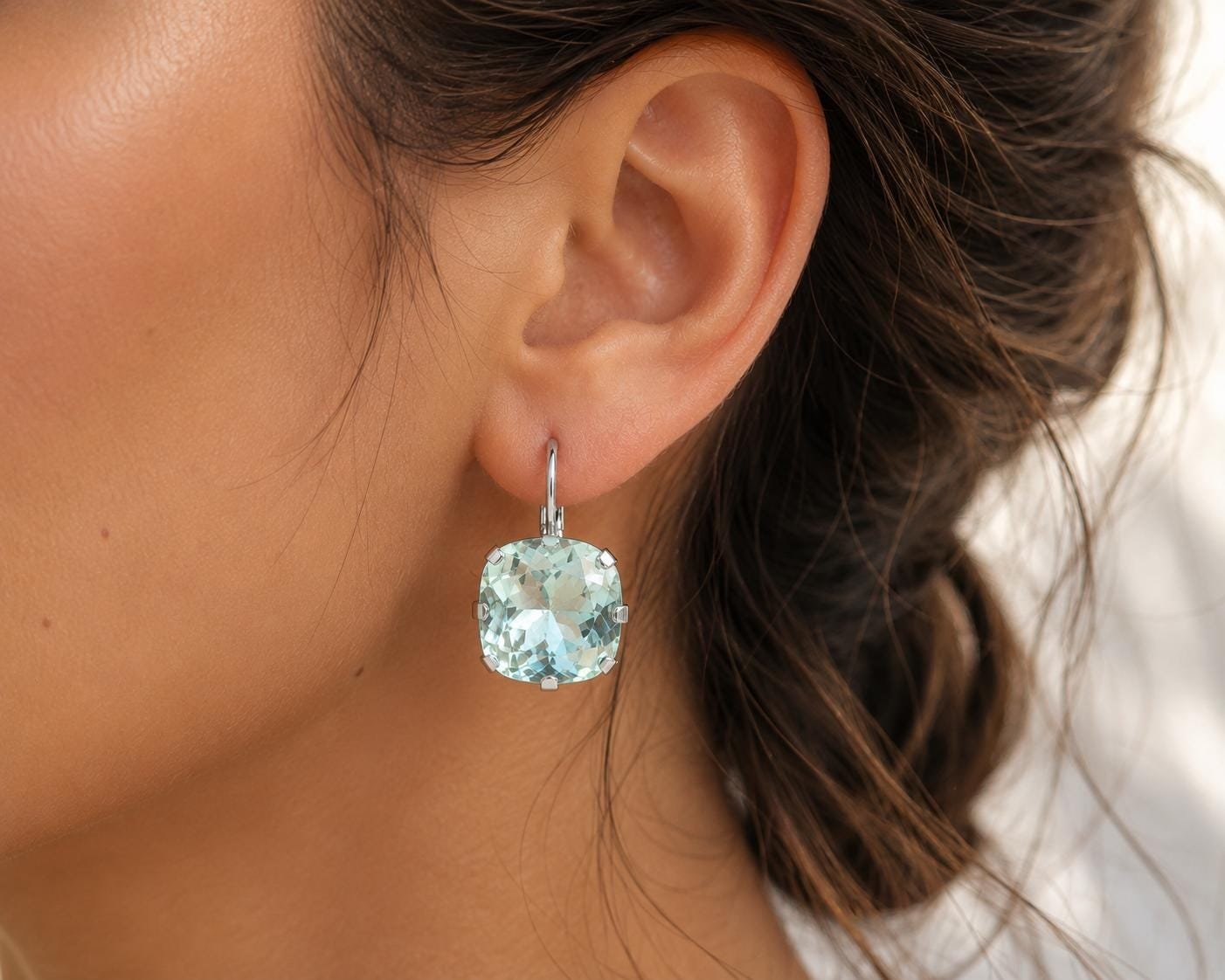 Cushion cut light shimmer blue crystal earrings in silver settings displayed on a model's ear, showing their elegant size and sparkle.