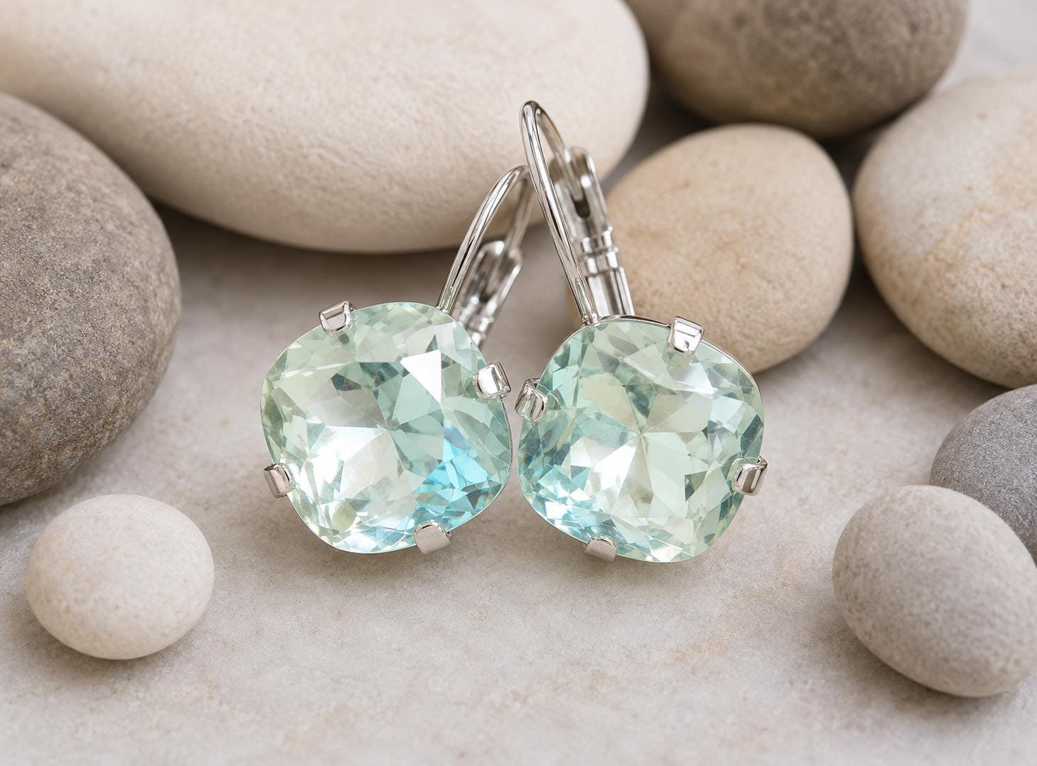 Close-up of handmade silver leverback earrings with cushion cut pale blue swarovski crystals sparkling in natural light.