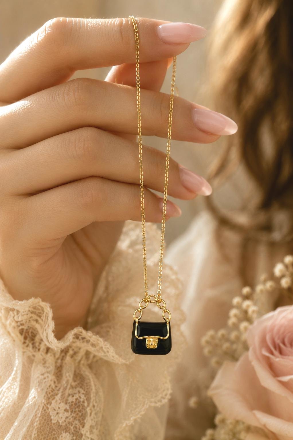 Stainless Steel Gold necklace with black purse pendant held between a woman's fingers.