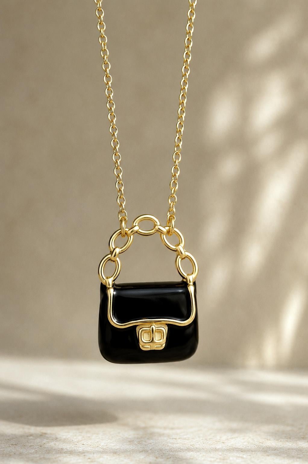 Black enamel purse pendant hanging from delicate gold chain.