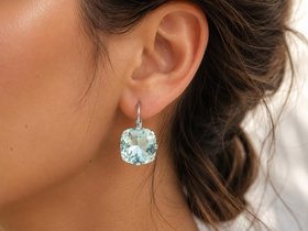 Cushion cut light shimmer blue crystal earrings in silver settings displayed on a model's ear, showing their elegant size and sparkle.